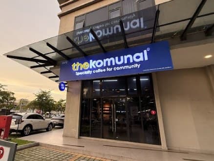 The Komunal Bukit Rimau storefront at dusk, blue signage over the glass entrance