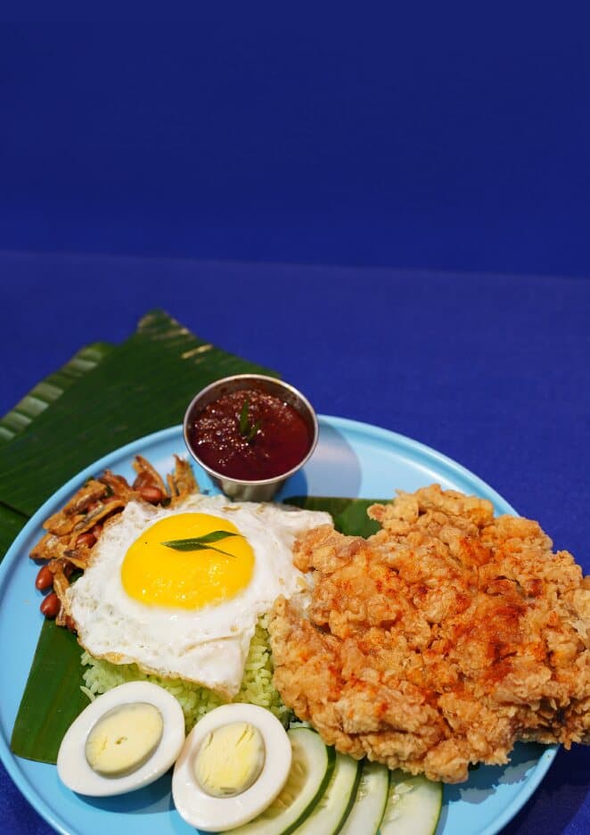 Nasi lemak pandan with a fried egg, crispy chicken, cucumber and boiled egg