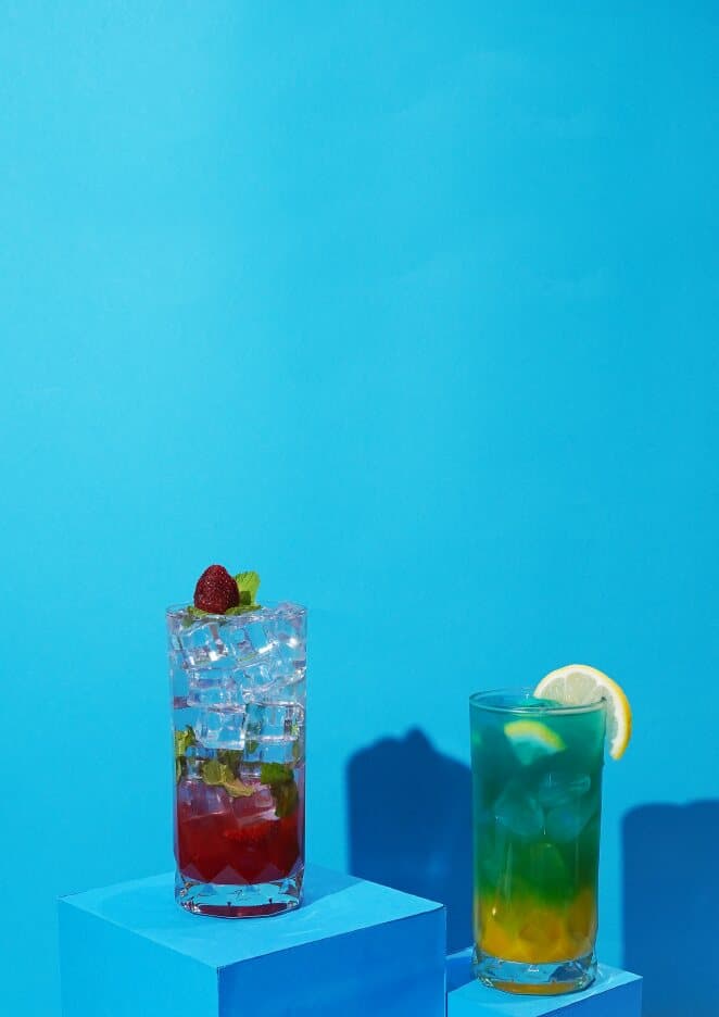 Two layered iced mocktails on blue blocks, one red and one blue-green