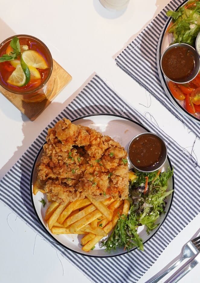 Fried chicken chop with fries, salad and sauce on a white plate